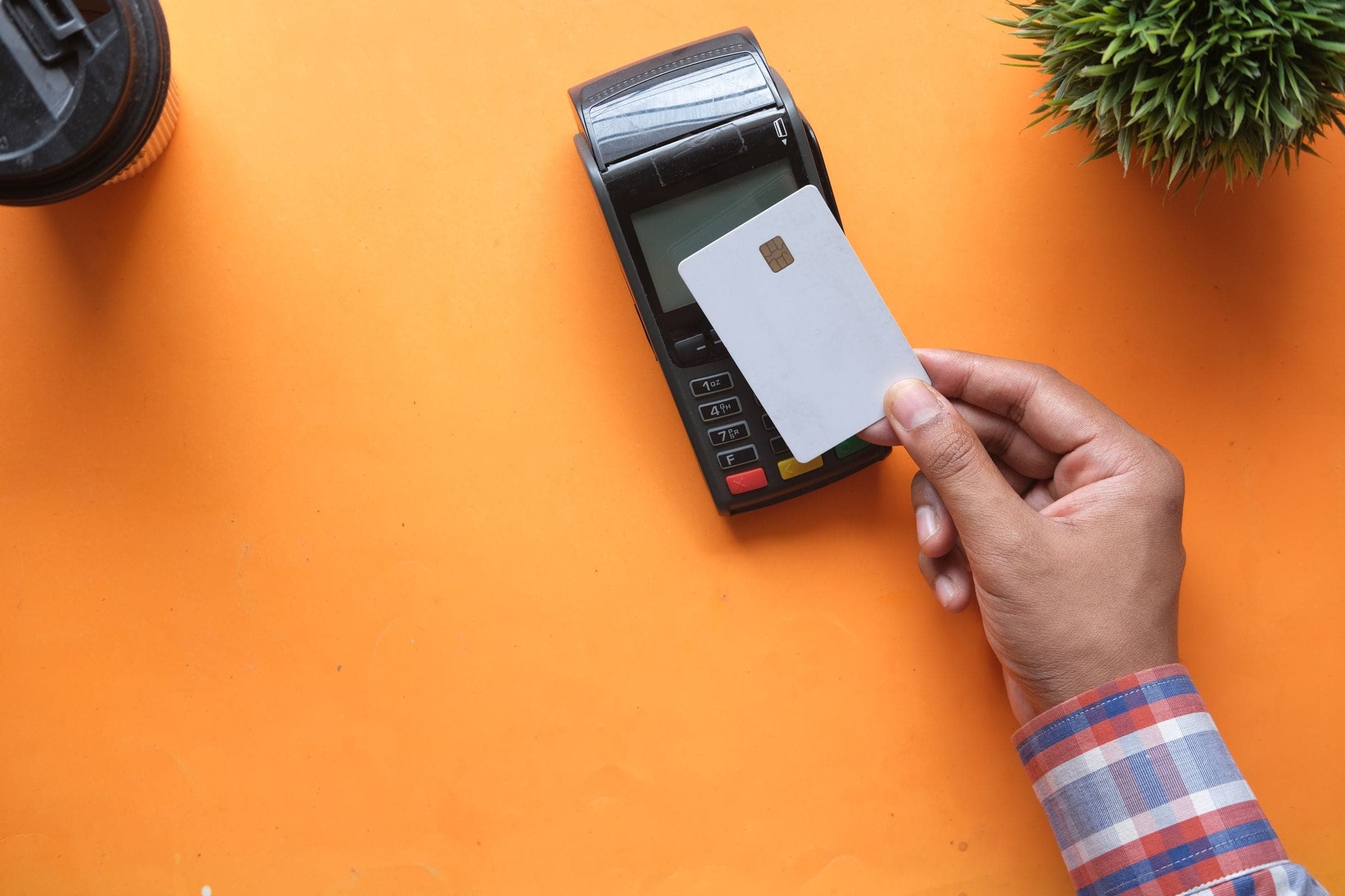 Hand houdt een betaalkaart bij een betaalautomaat op een oranje tafel